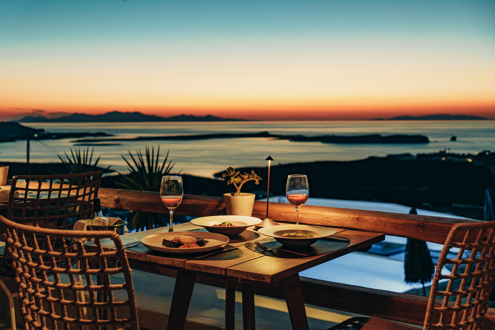 Candlelit dinner setting with wine and ocean sunset views in Paros