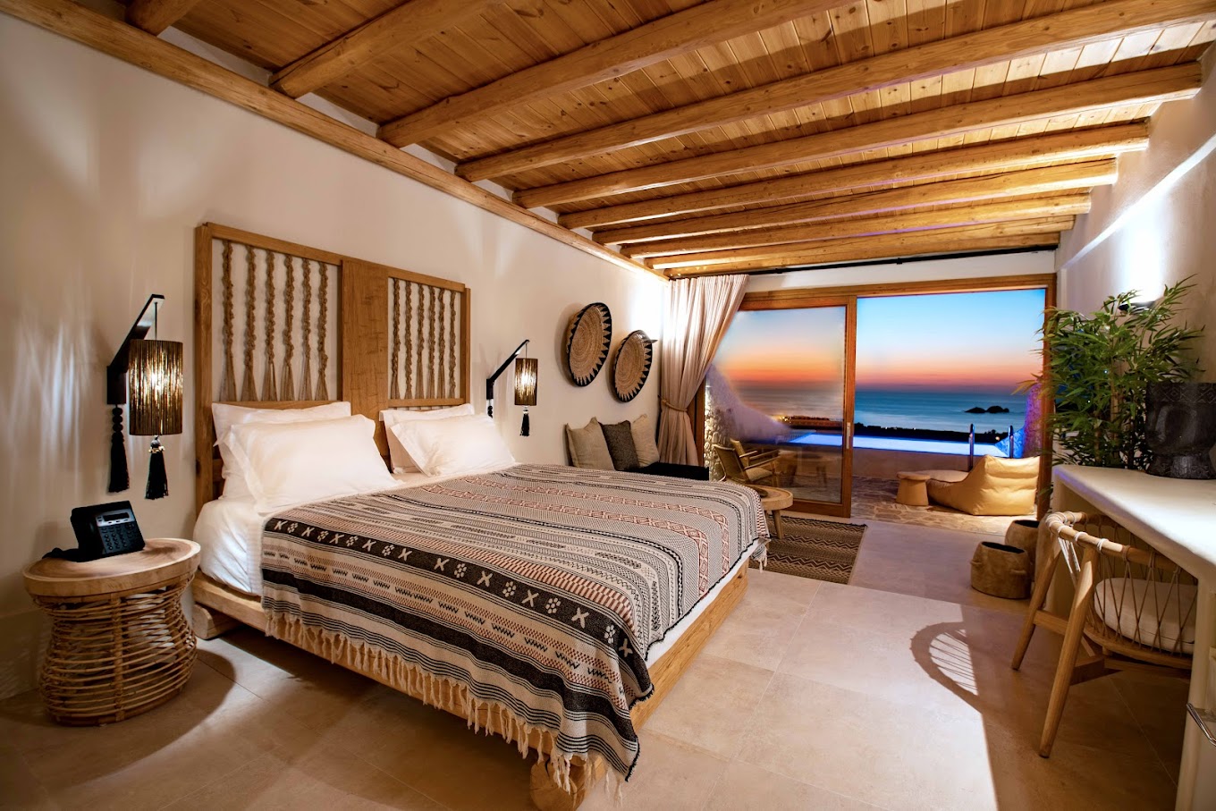 Warm wood-and-stone suite at Mythic Paros with an ocean-view terrace at sunset